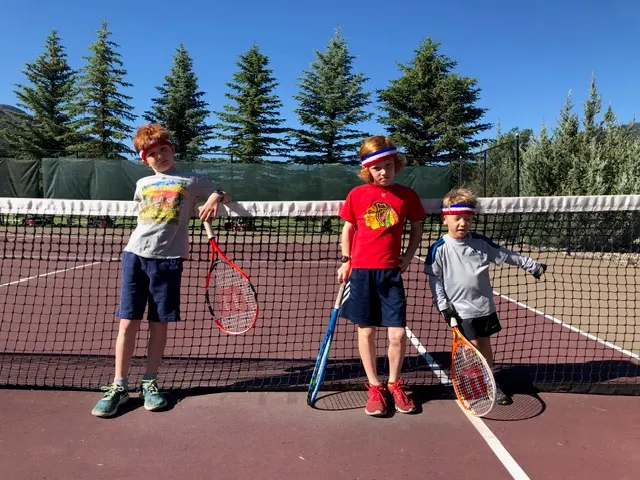 Three young Kids Camp players with racquets on the red clay tennis courts at Dalton Ranch