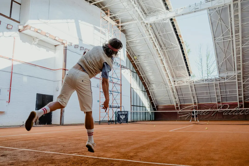 Tennis player practicing solo with ball machine on clay court